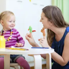 Radosna opieka nad zdrowym dzieckiem. Mama bawi się z córką pacynkami na palcach, rozwijając jej wyobraźnię.