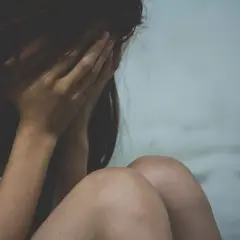 Kobieta ukrywa twarz w dłoniach, przygnębiona. Może to być związane z wypowiedzeniem umowy o pracę a zwolnieniem lekarskim od psychiatry.