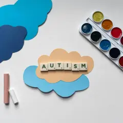 Litery układają słowo AUTISM na chmurce. Obok kredki i farby. Dzieci z autyzmem wysokofunkcjonującym mogą rozwijać się twórczo.