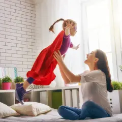 Mama rzuca córkę w stroju superbohaterki, która lata. To obraz prawdziwego rodzinnego kapitału opiekuńczego.