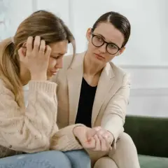 Kobieta w beżowym żakiecie pociesza smutną przyjaciółkę. Wsparcie w trudnych chwilach, jak opieka nad członkiem rodziny 14 dni kalendarzowych.