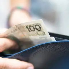 Dłoń wkłada banknot 100 zł do portfela. To może być część realizacji obowiązku alimentacyjnego.