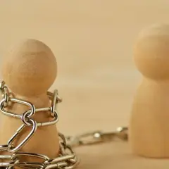Drewniany pionek skuty łańcuchem, obok drugi, wolny. Symbolizuje to techniki manipulacji i kontroli.