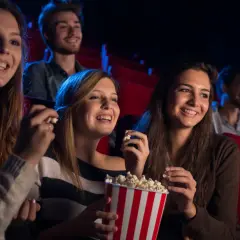 Uśmiechnięci ludzie w kinie, jedzący popcorn. Czy to Cinema City bilet rodzinny co to?