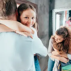 Dziewczynka mocno przytula tatę, jej uśmiech świadczy o dobrym samopoczuciu i zdrowej psychice. Mama tuli synka w tle.