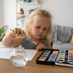 Dziewczynka z blond włosami maluje farbami. Jej skupienie może być jednym z objawów autyzmu u 2 latka, gdy dziecko angażuje się w powtarzalne czynności.