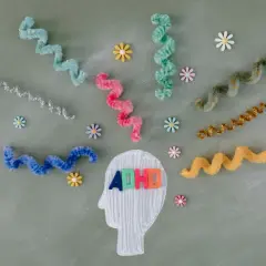 Kolorowe litery "ADHD" w głowie symbolizują diagnozę. Wirujące wstążki i kwiatki odzwierciedlają natłok myśli.