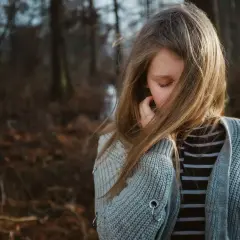 Smutna dziewczynka w lesie, jej włosy zasłaniają twarz. Czuła, że antydepresanty zniszczyły jej życie, odbierając radość.