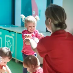 Wesoła dziewczynka z kitkami, w różowej bluzce, pokazuje coś dorosłej osobie. Widać też inne dzieci. To pokazuje, jak różny jest temperament co to.