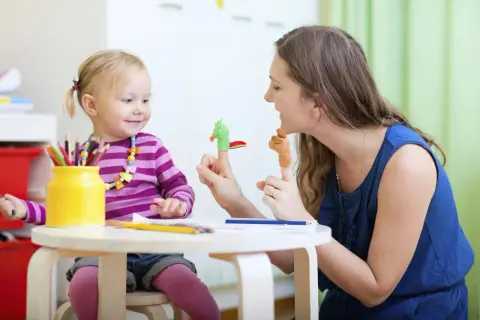 Radosna opieka nad zdrowym dzieckiem. Mama bawi się z córką pacynkami na palcach, rozwijając jej wyobraźnię.