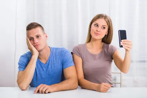 Znudzony chłopak obok dziewczyny robiącej selfie. Czy to objawy NPD?