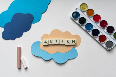Litery układają słowo AUTISM na chmurce. Obok kredki i farby. Dzieci z autyzmem wysokofunkcjonującym mogą rozwijać się twórczo.