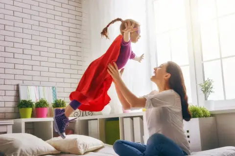 Mama rzuca córkę w stroju superbohaterki, która lata. To obraz prawdziwego rodzinnego kapitału opiekuńczego.