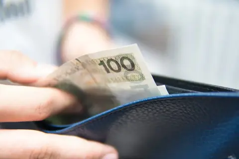 Dłoń wkłada banknot 100 zł do portfela. To może być część realizacji obowiązku alimentacyjnego.