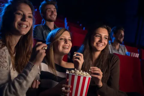 Uśmiechnięci ludzie w kinie, jedzący popcorn. Czy to Cinema City bilet rodzinny co to?