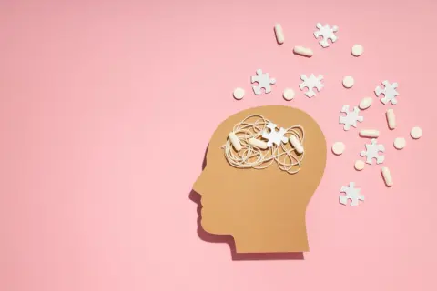 Symboliczne przedstawienie problemów z koncentracją i myśli w głowie, sugerujące poszukiwanie odpowiedzi na pytanie jak leczyć ADHD. Pigułki i puzzle symbolizują leczenie.