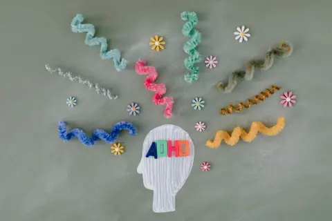 Kolorowe litery "ADHD" w głowie symbolizują diagnozę. Wirujące wstążki i kwiatki odzwierciedlają natłok myśli.