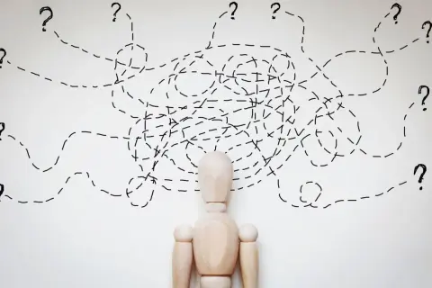 Drewniany manekin z chaotycznymi liniami i znakami zapytania nad głową, symbolizujący osobowość chwiejną emocjonalnie.