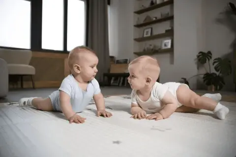Dwa niemowlaki na macie, jedno w niebieskim, drugie w białym body, patrzą na siebie. Ich mimika może sugerować niestabilność emocjonalną.