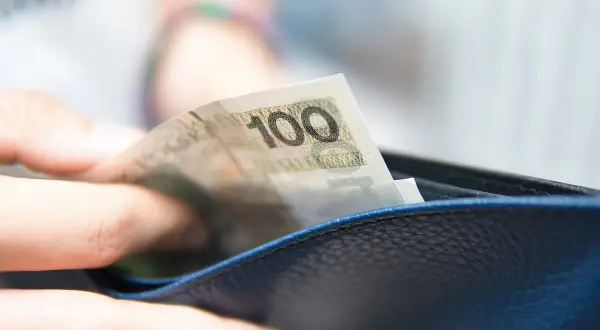 Dłoń wkłada banknot 100 zł do portfela. To może być część realizacji obowiązku alimentacyjnego.