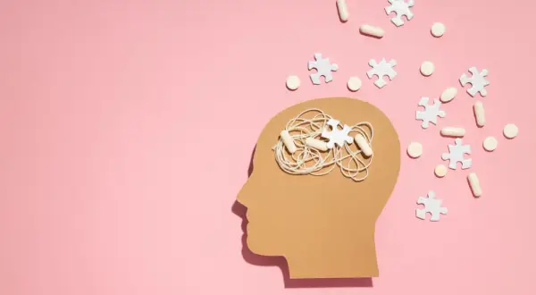 Symboliczne przedstawienie problemów z koncentracją i myśli w głowie, sugerujące poszukiwanie odpowiedzi na pytanie jak leczyć ADHD. Pigułki i puzzle symbolizują leczenie.