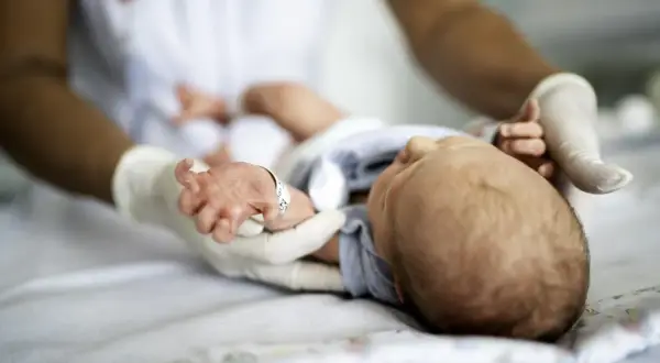 Delikatne badania neurologiczne noworodka. Ręce w rękawiczkach badają maleńkie dłonie i stopy dziecka.