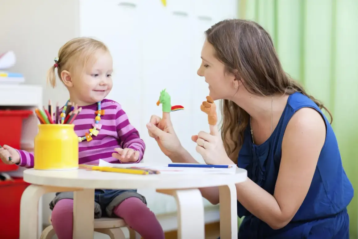 Radosna opieka nad zdrowym dzieckiem. Mama bawi się z córką pacynkami na palcach, rozwijając jej wyobraźnię.