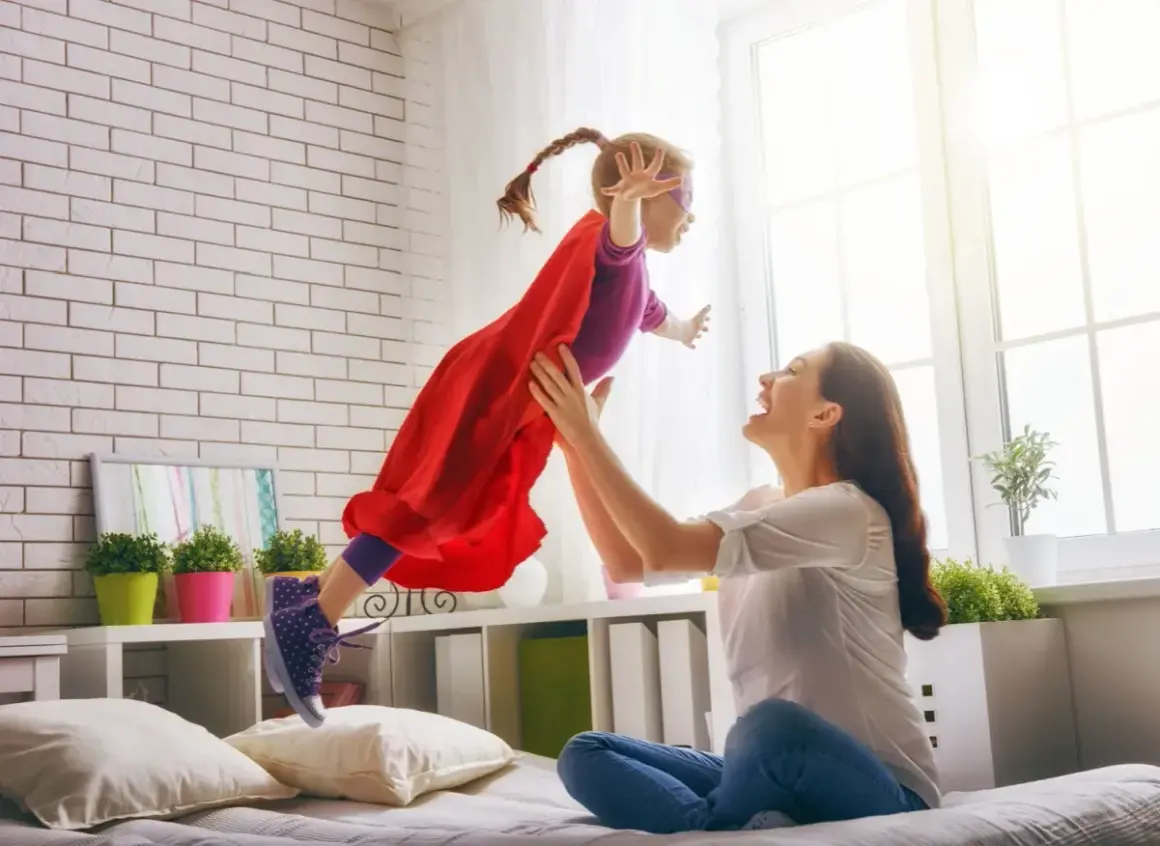 Mama rzuca córkę w stroju superbohaterki, która lata. To obraz prawdziwego rodzinnego kapitału opiekuńczego.