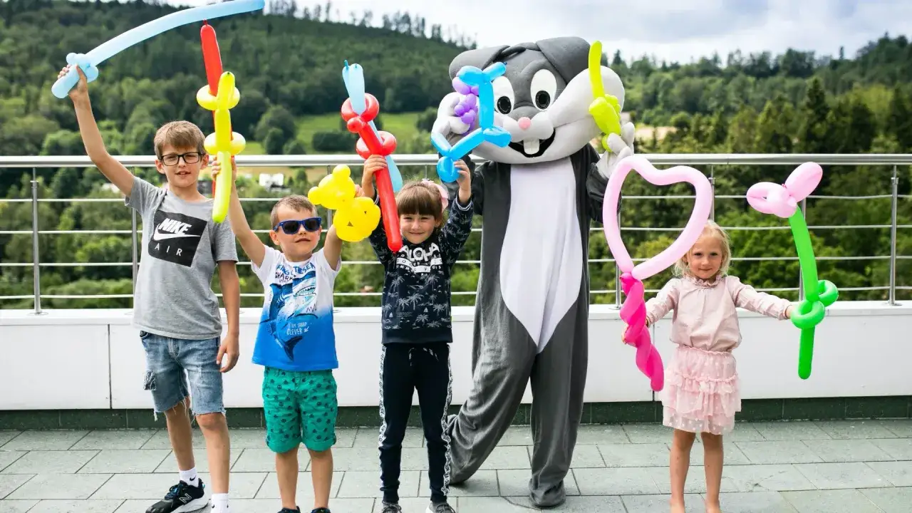 Postać z bajki, królik, trzyma balony. Dzieci też mają balony w kształcie mieczy i serca.