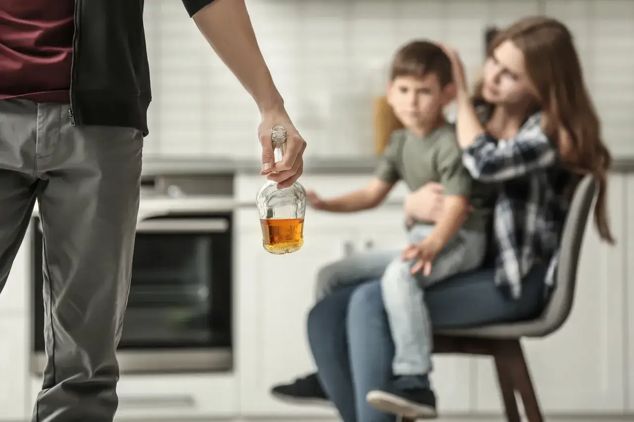 Smutne dzieci alkoholików, matka tuli synka, ojciec trzyma butelkę.
