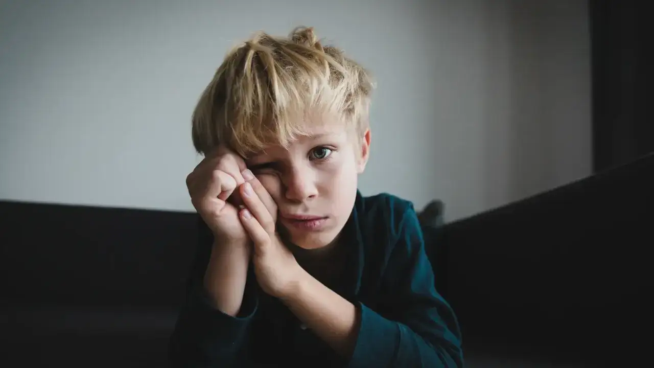 Chłopiec z blond włosami, zamyślony, z rękami przy twarzy. Obraz symbolizuje trudności w komunikacji, często spotykane przy asperger u dzieci.