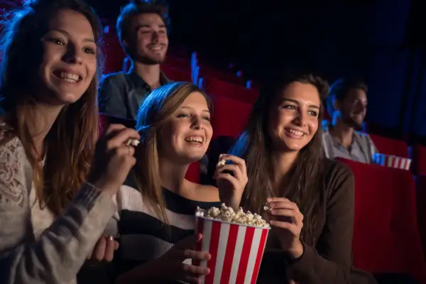 Uśmiechnięci ludzie w kinie, jedzący popcorn. Czy to Cinema City bilet rodzinny co to?